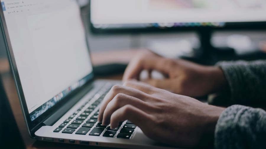 Detal pracy — dłonie przy klawiaturze laptopa w naturalnym świetle.