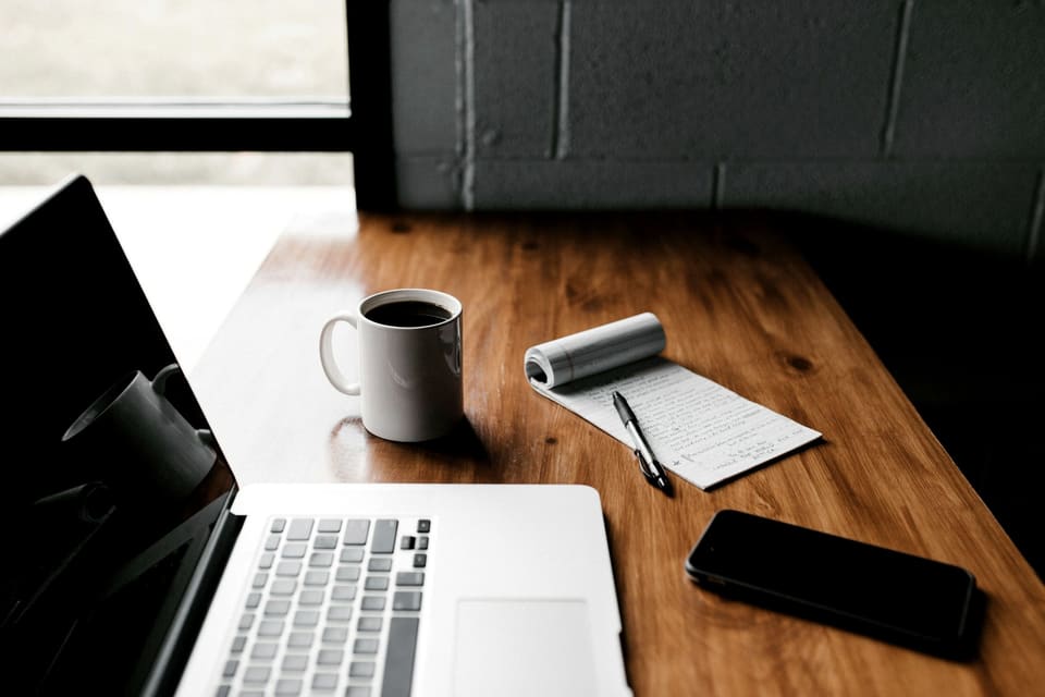 Biurko studia — laptop, notatnik i kawa w ciepłym świetle.